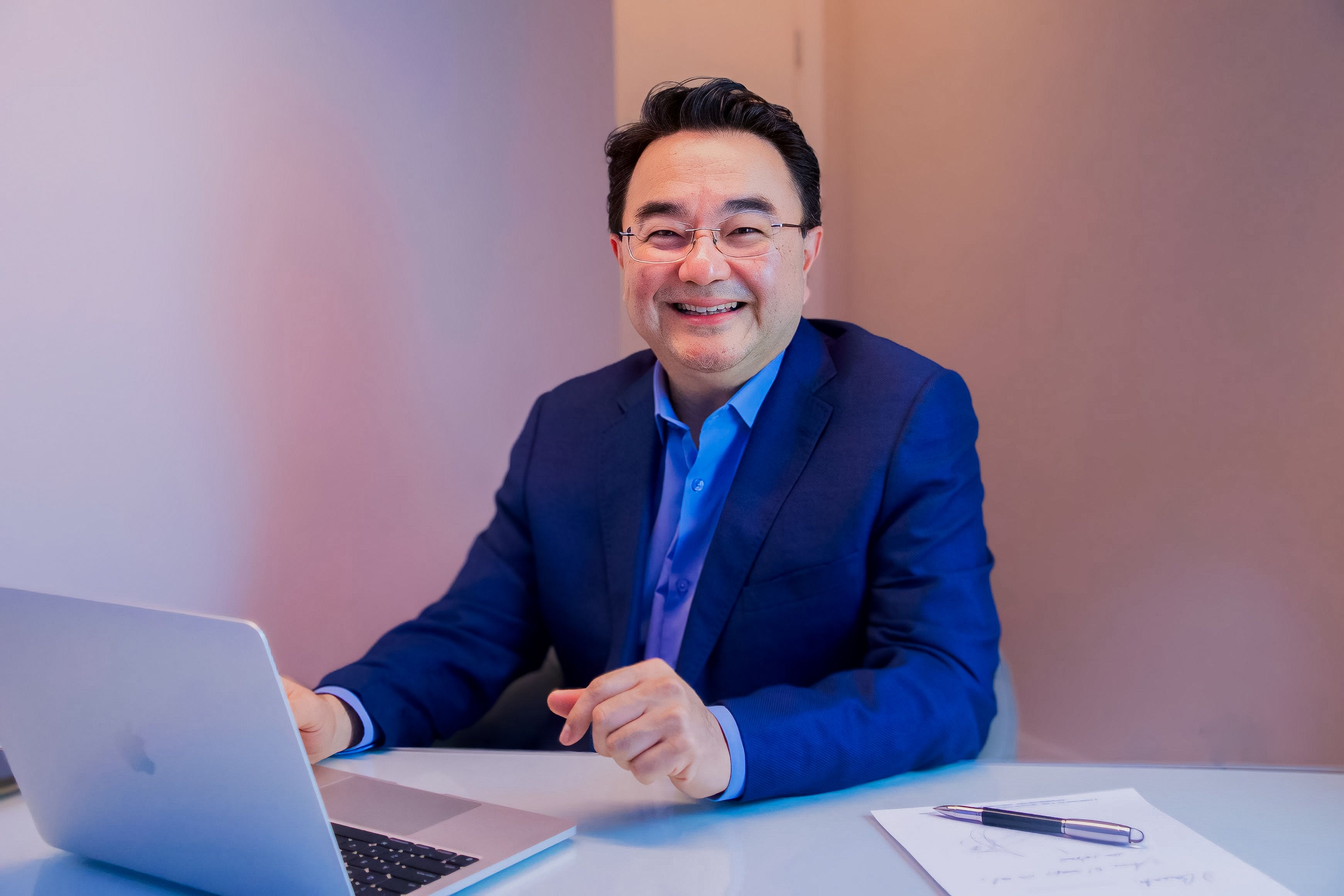 Dr. Fábio Sakae, ginecologista e especialista em reprodução humana, sorrindo na mesa de sua clínica em São Paulo